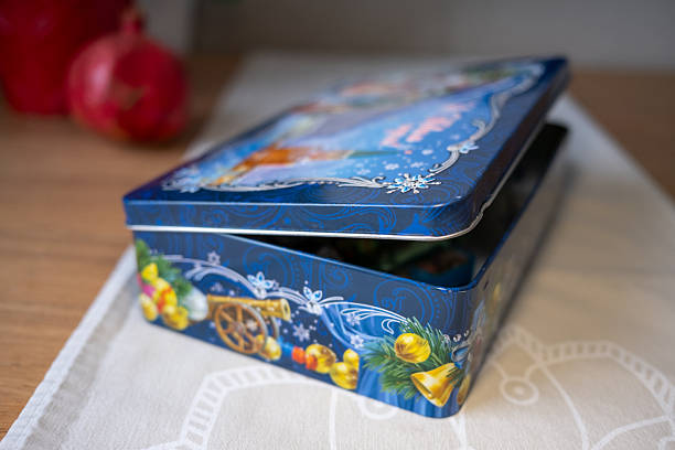 Close-up of an open blue Christmas gift tin filled with sweets. Selective focus on the festive design with bells and ornaments creates a cozy, celebratory atmosphere with a blurred background.