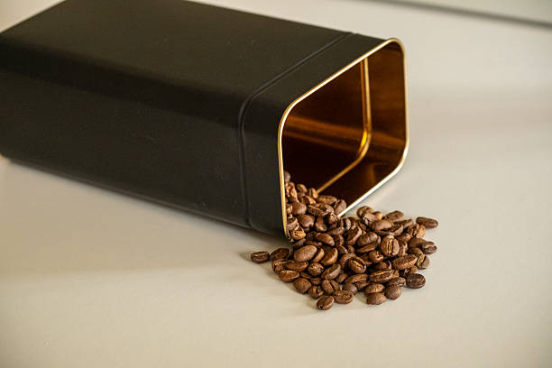 Coffee Beans Pouring into a Black Metal Container on a White Surface,close up