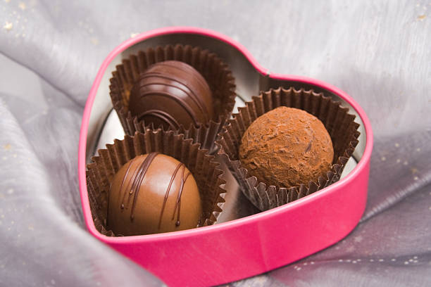 Three delicious truffle chocolates in a heart shaped tin can on folds of chiffon